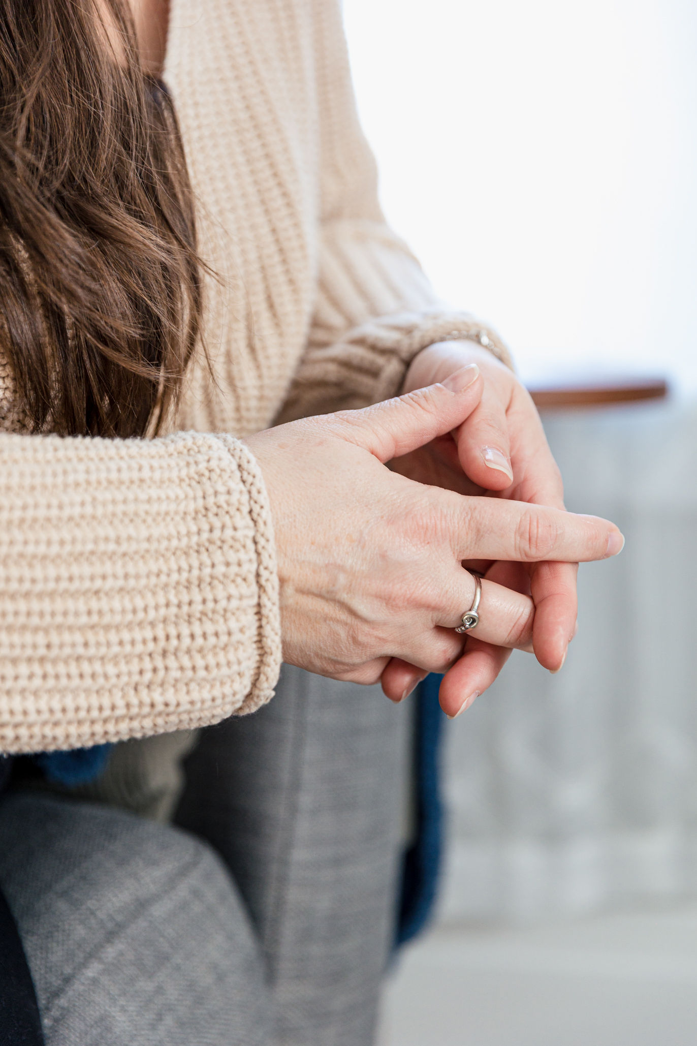 A close-up of a person wearing a beige knit sweater with hands resting on their lap, showing a silver ring with a small stone—capturing a peaceful moment at Therapeutic Family Connections in York. The person's long brown hair is partially visible.