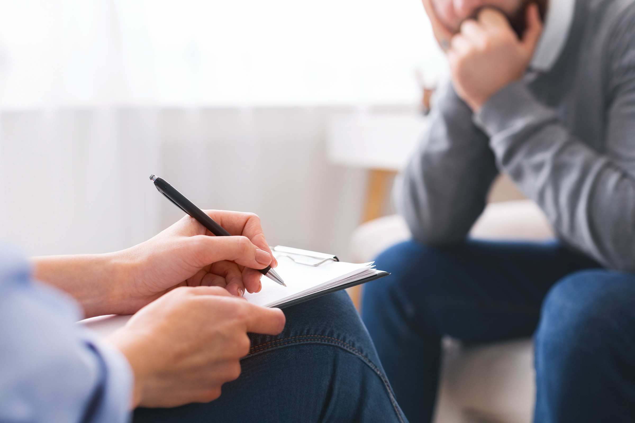 During a co-parenting counseling session at Therapeutic Family Connections in York, a person holding a clipboard and pen takes notes while another sits across from them, appearing thoughtful or concerned during their conversation.